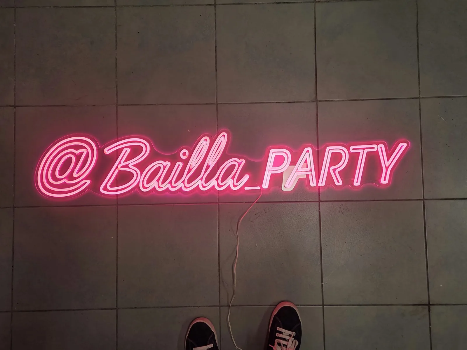 Różowy neon LED z nazwą profilu Bailla Party, pisany odręczną czcionką, położony na płytkach w pracowni