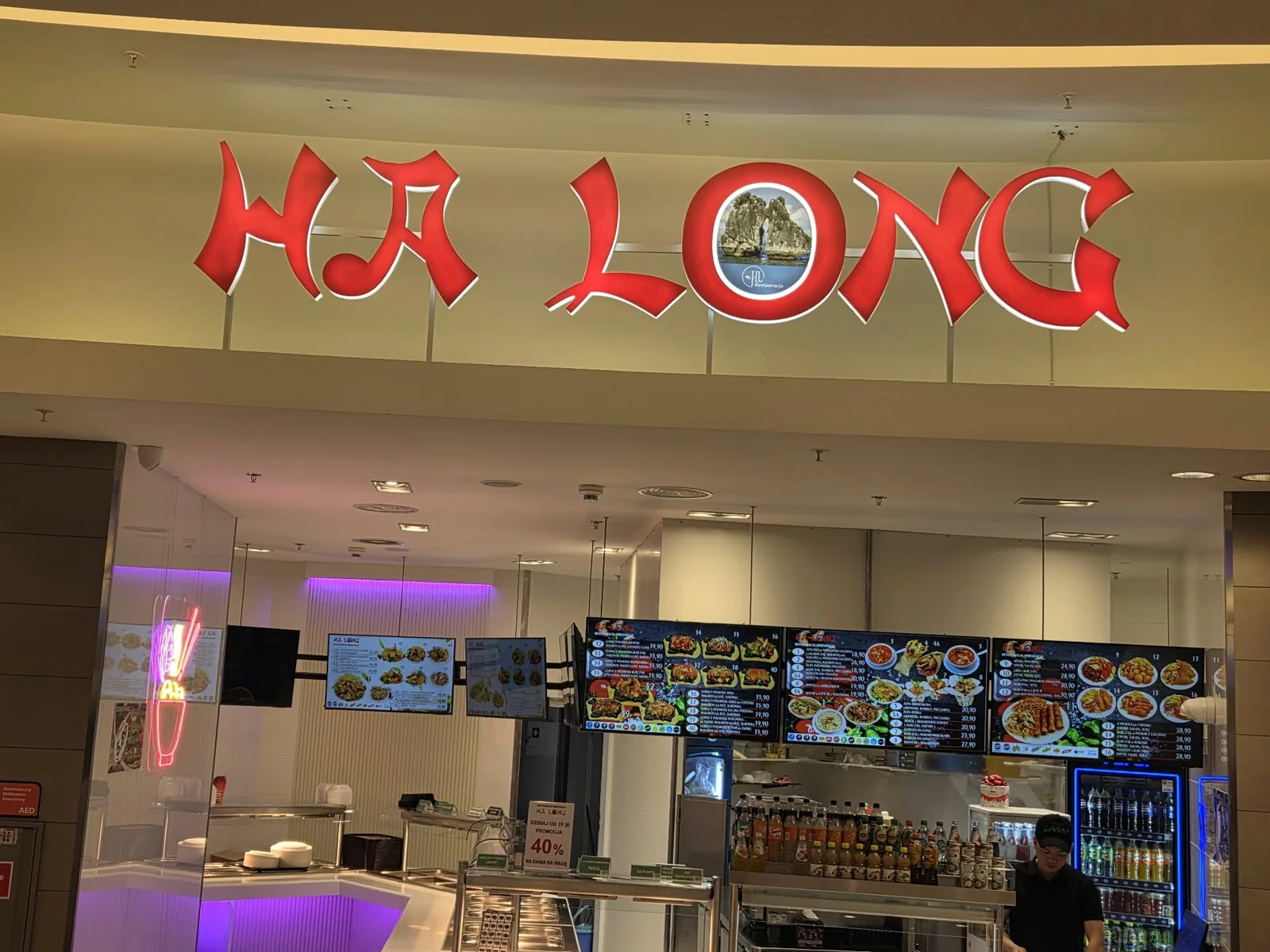 Czerwone litery przestrzenne „HA LONG” nad wejściem do restauracji w galerii handlowej, obok neon LED z miską ramenu