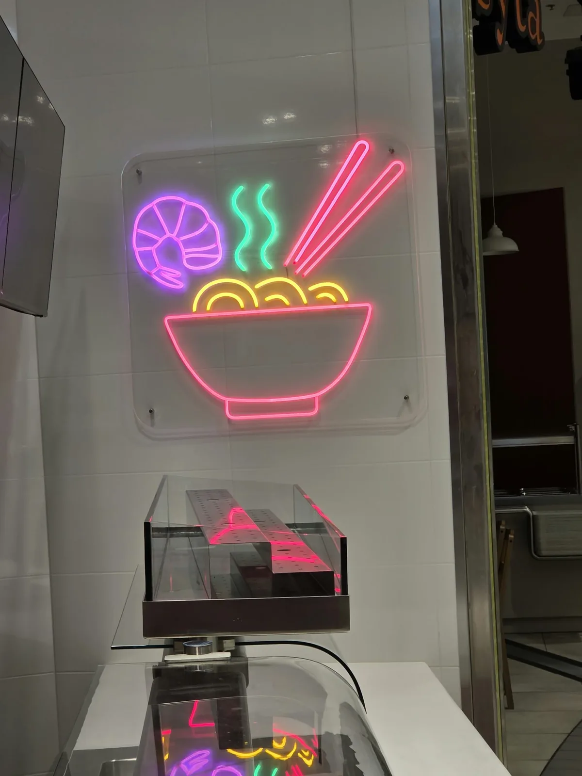 Neon LED z miską ramenu na przezroczystej pleksi nad ladą restauracji, widoczny zza szklanej ściany