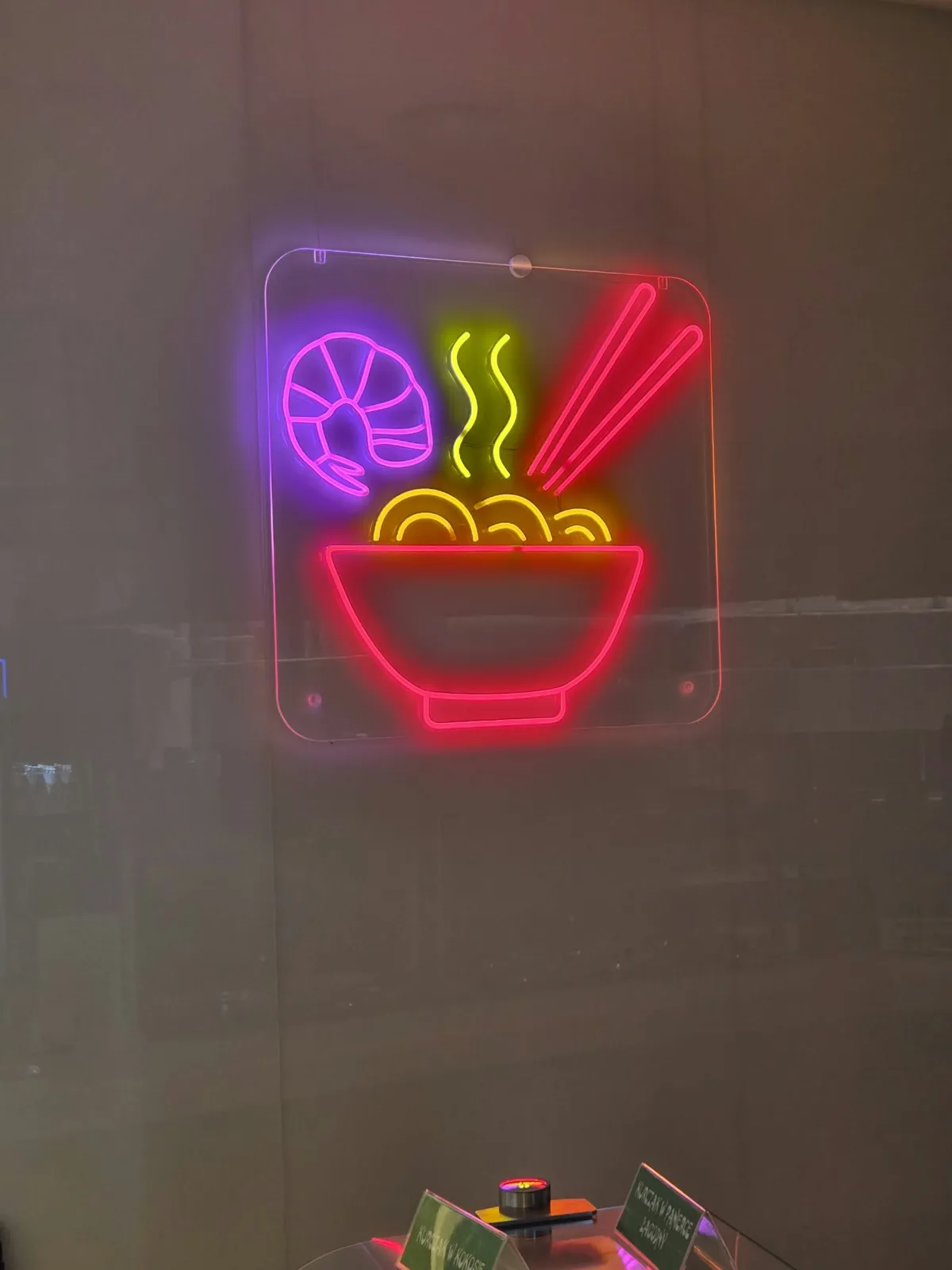 Wielokolorowy neon LED — miska ramenu z krewetką, pałeczkami i parą — na przezroczystej pleksi zawieszonej na szybie